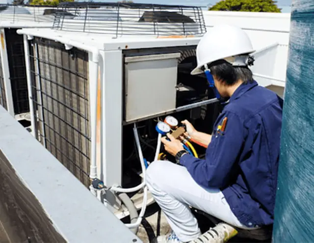 Technician with manifold gauges at a rooftop HVAC unit