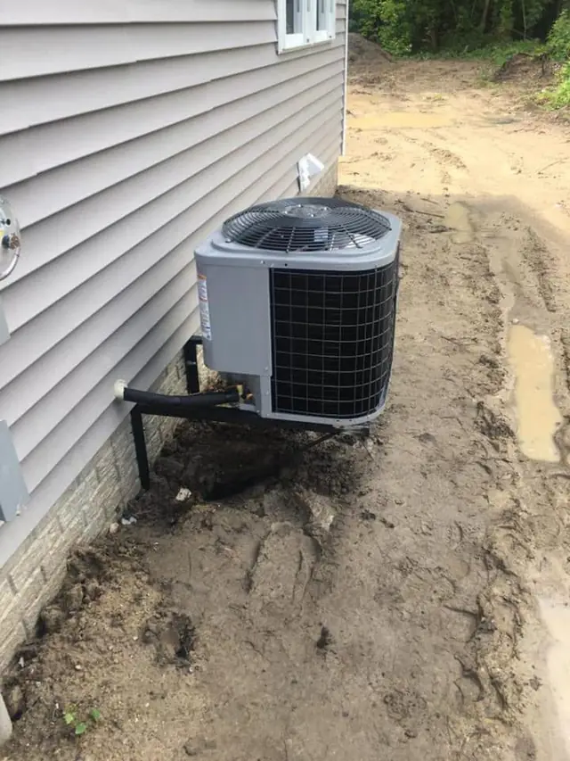 Condenser unit mounted on a bracket beside a house on a fresh job site